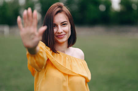 Brunette with a Smile on her Face put her palm forward, Portrait on a Natural Background. Green grass and hand in soft focus. stop conceptの写真素材