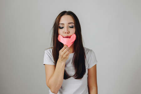 Brunette blows on a pink mask against a white background. Girl Corrects the protective mask on her...