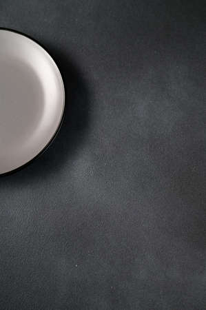 Empty blank gray ceramic round plate or dish on black stone background with copy space. Top view of traditional handcrafted kitchenware conceptの写真素材
