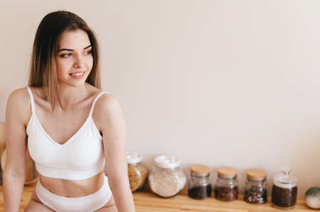 Sexy Young Woman Sits Kitchen Table Leaning Forward and Looking out Window. Girl in white underwear...