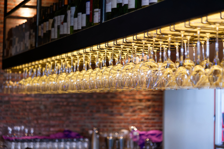 Group of empty wine glasses hanging from metal beams in a barの写真素材