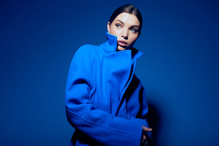 fashion portrait of young elegant woman in blue coat on blue backgroundの写真素材
