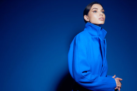 fashion portrait of young elegant woman in blue coat on blue backgroundの写真素材