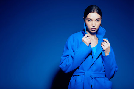 fashion portrait of young elegant woman in blue coat on blue backgroundの写真素材