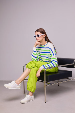 Fashion portrait of young woman in striped green sweater and pants. Sunglasses, white sneakers,...