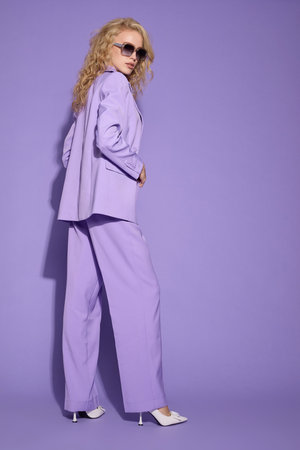 Fashion female model in lilac suit, white shoes, top and sunglasses. Total fashion look. Lilac background. Young blond curly woman.の写真素材