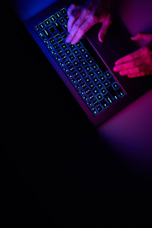 Male hands are typing on a laptop keyboard. A man works, develops a business, studies, plays a computer game at night. Close-up view.の写真素材
