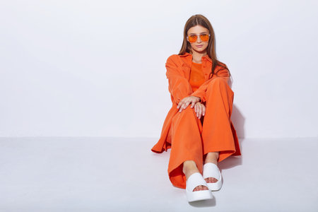 Young fashion woman in orange pants orange top orange shirt on white background. Platform slides sandals, orange sunglasses.の写真素材