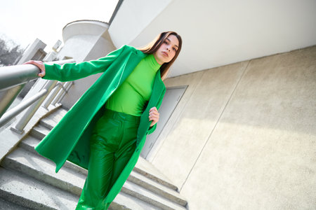 High fashion photo of a young brunette woman in green coat, poloneck and leather pants. Urban street fashion. Monochrome green outfitの写真素材