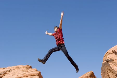 Handsome young man jumping on red rocksの写真素材