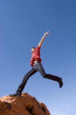 Handsome young man jumping on red rocksの写真素材