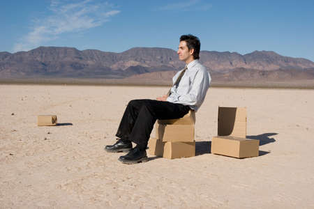 Businessman sitting on boxes in the desertの写真素材