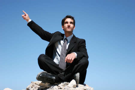 Businessman in black suit sitting on the rocksの写真素材