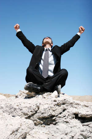 Businessman in black suit sitting on the rocksの写真素材