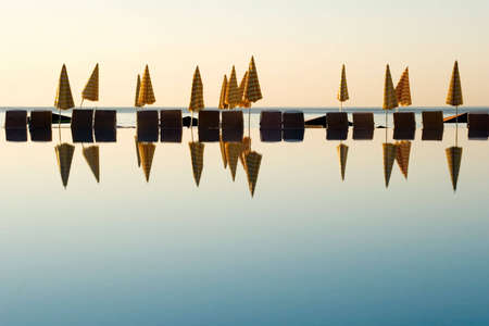 Lined up umbrellas reflecting on water during sunriseの写真素材