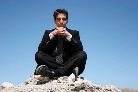 Businessman in black suit sitting on the rocksの写真素材