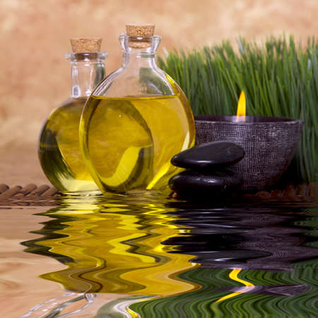 Relaxing candle and massage oil bottles front of green grassの写真素材