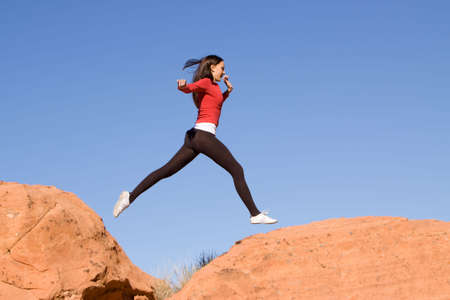 Beautiful young athletic woman running and jumping on red rocksの写真素材