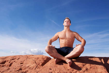 Muscular man meditating on red rocksの写真素材