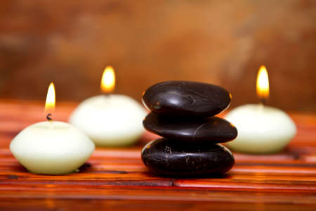 Hot spa stones and lit candles on bamboo matの写真素材