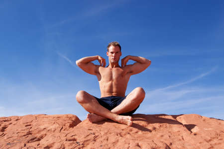 Muscular man meditating on red rocksの写真素材