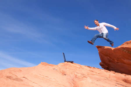 Young man outdoors with his laptop jumping on red rocksの写真素材