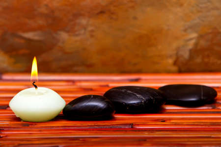 Hot spa stones and lit candles on bamboo matの写真素材