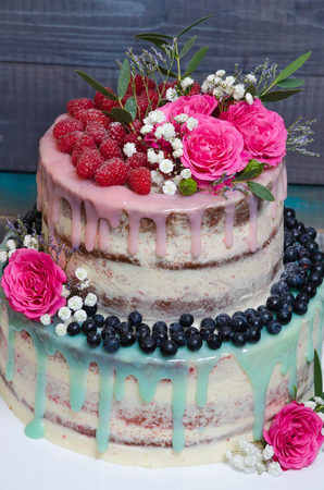 wedding color drip cake with roses, blueberries and  raspberries on wooden plankの写真素材