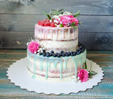 wedding color drip cake with roses, blueberries and  raspberries on wooden plankの写真素材