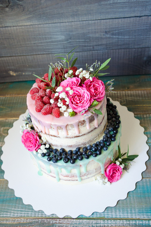 wedding color drip cake with roses, blueberries and  raspberries on wooden plankの写真素材