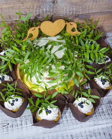 a wedding cake with topper and cupcakes decorated with greeneryの写真素材