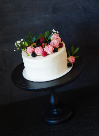 a Cream cheese wedding cake with cupcakes decorated with berries and flowersの写真素材