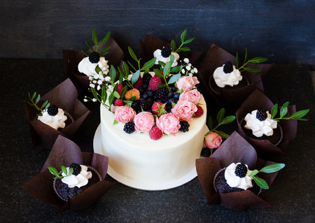 a Cream cheese wedding cake with cupcakes decorated with berries and flowersの写真素材