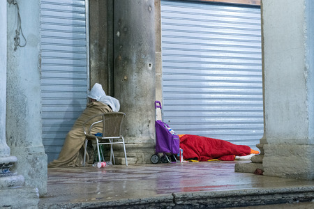 two people sleeping on the street covered with cold, one sat on the chair and another lying on the groundの写真素材