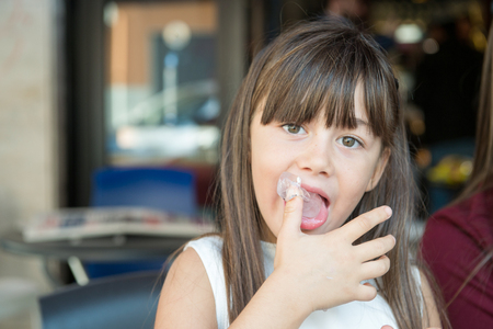 small little girl licks his fingers made of ice creamの写真素材