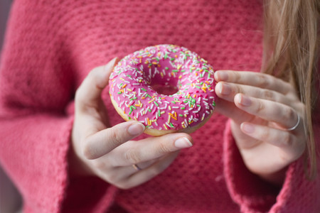 Doughnut in a pink glaze in the hands of the girl on a background of a pink sweater. Photo girl without a face.の写真素材