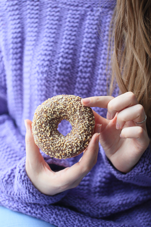 Donut with chocolate and nuts in the hands of a girl close-up. Only hands on background svitora. Photo without a face.の写真素材