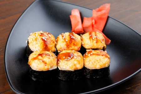 Appetizing baked hot sushi rolls. Set sushi on a black plate with ginger closeup.の写真素材