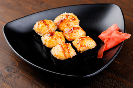 Appetizing baked hot sushi rolls. Set sushi on a black triangular plate with ginger closeup.の写真素材