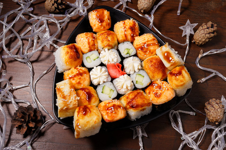 New Year's assortment of sushi on a black plate, with garlands. Christmas New Year sushi set.の写真素材