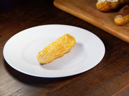 One eclair on a white plate, on a dark wooden background. Homemade baking.の写真素材