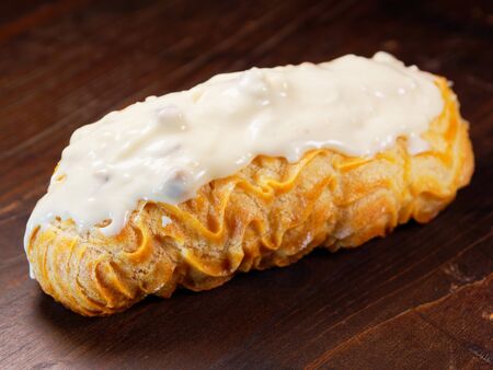 Eclair with white chocolate icing. One eclair on a wooden vintage background.