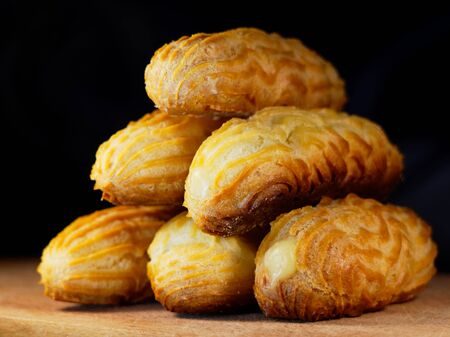 A stack of eclairs without glaze. Eclairs on a wooden background. Group of cakes, home baking.