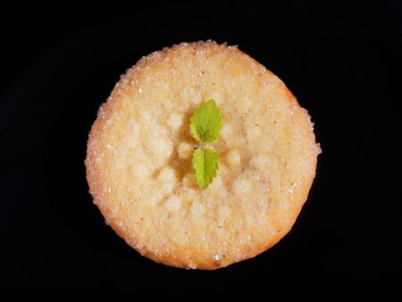Appetizing sugar cookies on a black background. One cookie with lemon balm, top view.の写真素材
