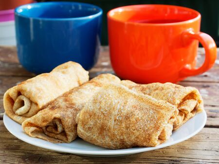Morning rustic breakfast. Pancakes rolled up on a white plate. Two bright cups of tea, romantic breakfast in the village.の写真素材