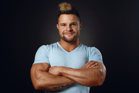 Studio portrait of a muscular sportsman in a blue t-shirt smiling over black backgroundの写真素材
