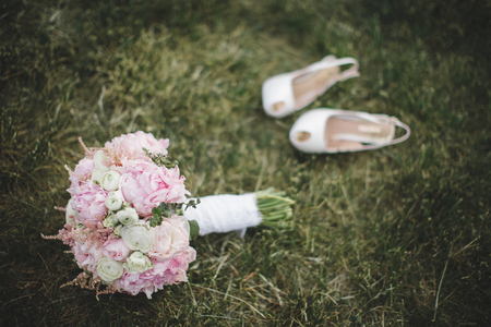 Beautiful  wedding bouquet and a pair of white shoes laying on the green lawnの写真素材