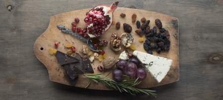 Variety of fresh fruits, sweets and cheeses shot from above an wooden boardの写真素材