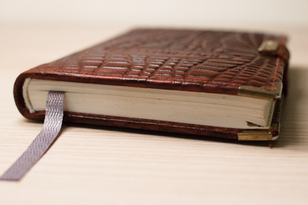 Handheld notebook in a brown leather cover on the background of a wooden tableの写真素材