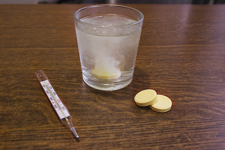 A glass with water, tablets and a thermometer on the tableの写真素材